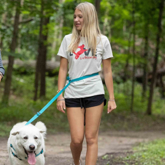 Two women walking dogs on a trail in a forested area