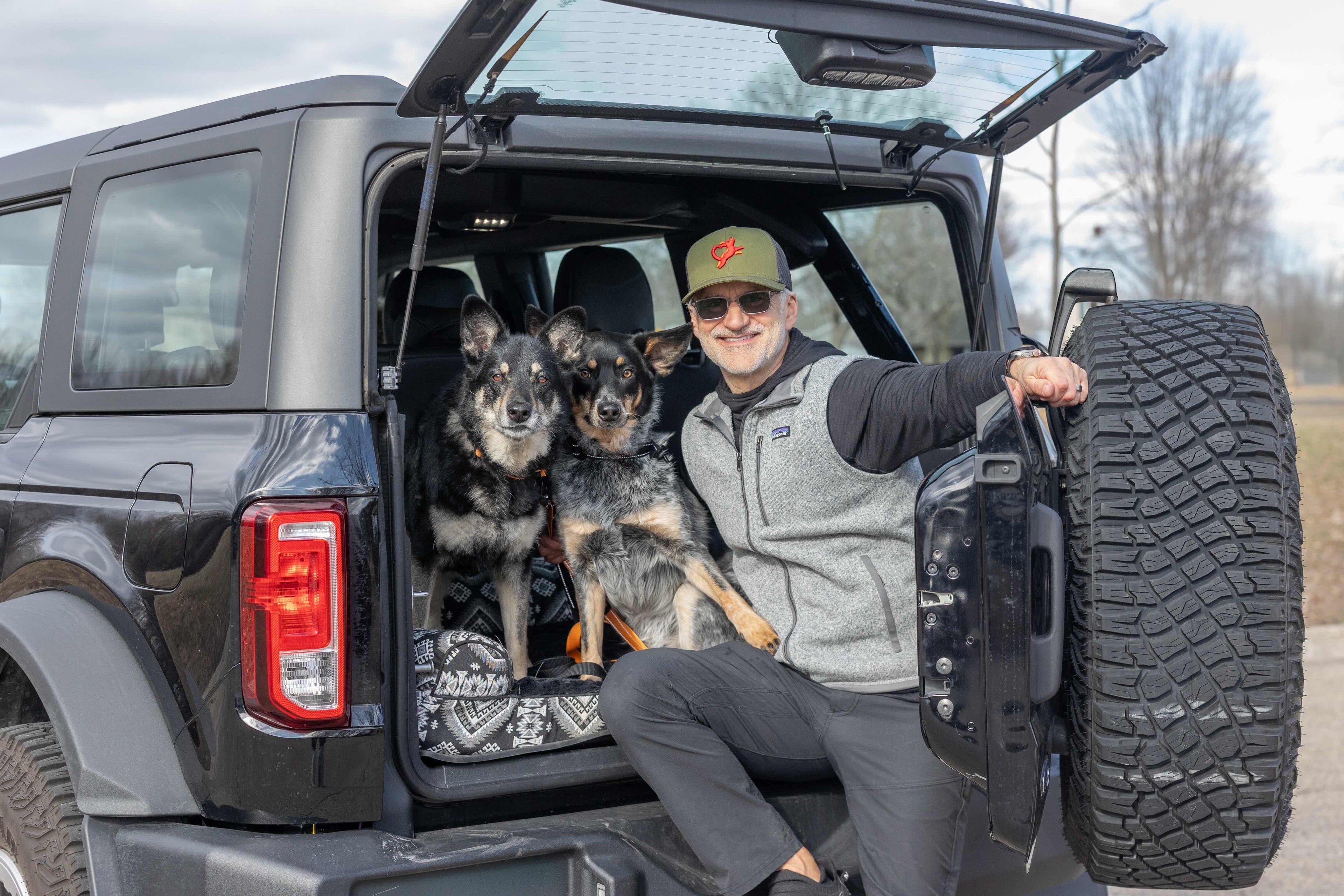 Person with two dogs in the back of an open SUV on a cloudy day.