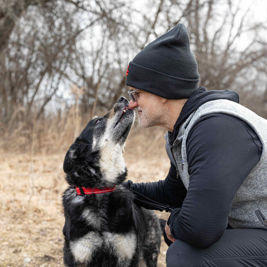 Man in outdoor setting with a dog, both looking at each other.