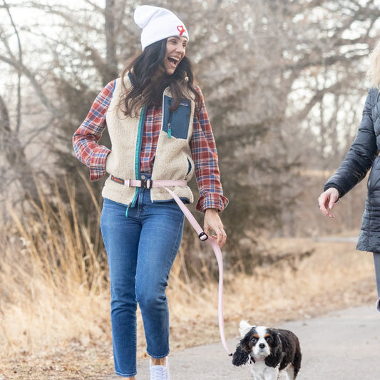 Two women walking their dogs on a path in a park during autumn.