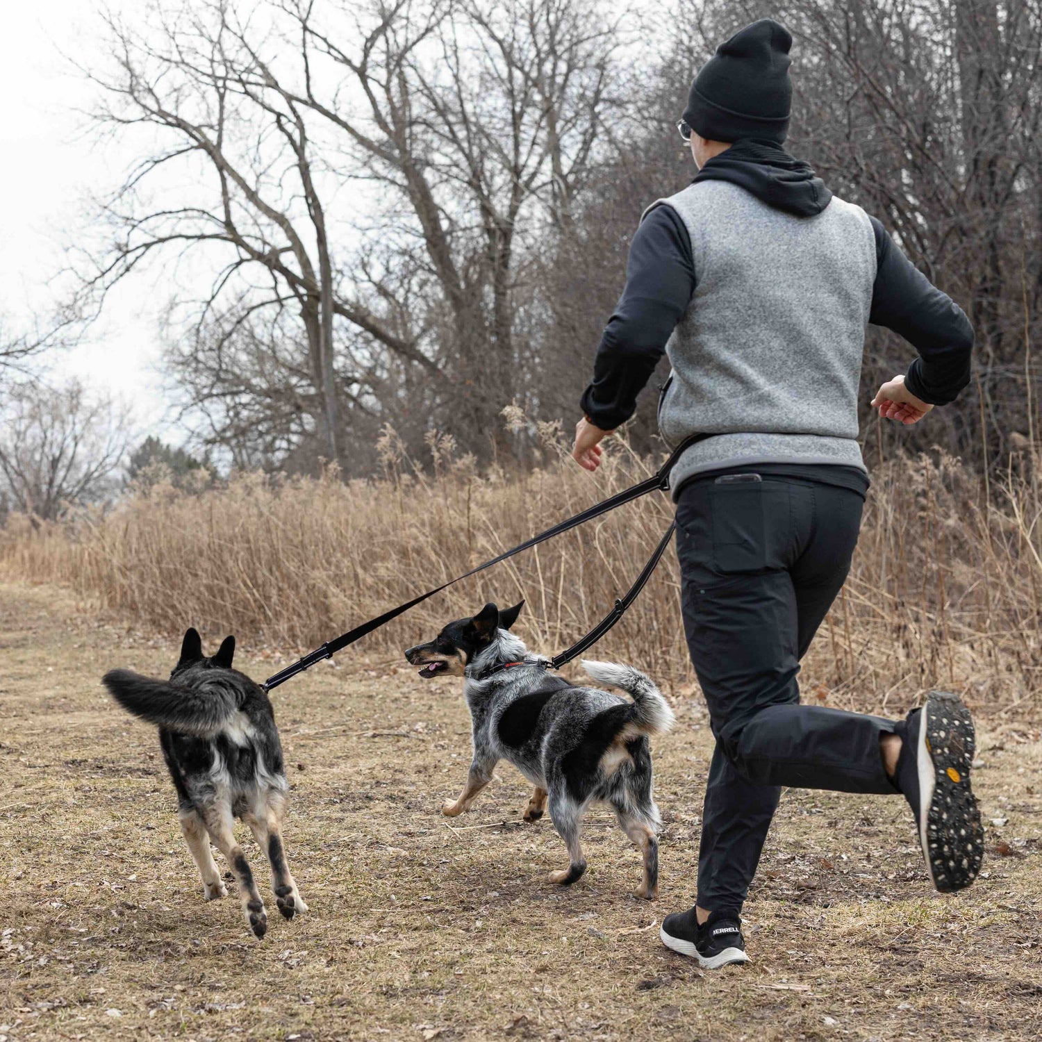 Person running with two dogs on a path in a wooded area