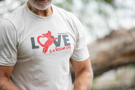 Person wearing a white t-shirt with a graphic and text 'LOVE is a Rescue Dog' outdoors.
